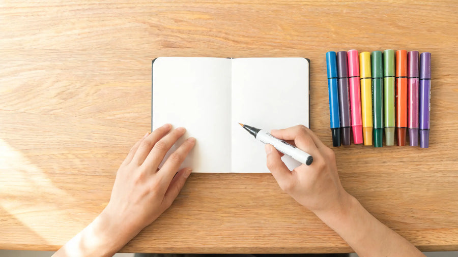 Main d'artiste tenant un marqueur acrylique au-dessus d'un carnet, démonstration des gestes de base pour débutants
